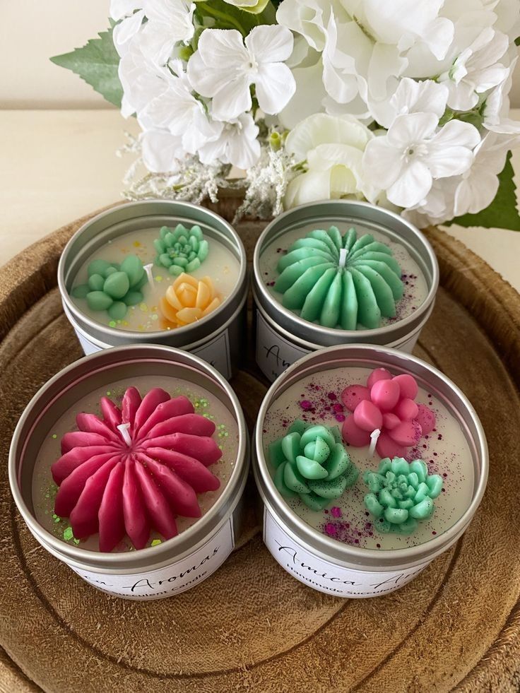 four tins filled with candles sitting on top of a wooden tray next to flowers