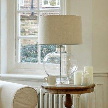 a glass table with a lamp on it next to a chair and window sill