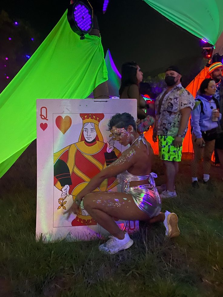 a man sitting on the ground in front of a painting with people standing around him