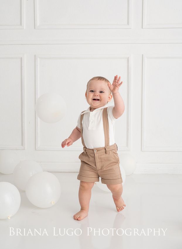 a baby standing in front of white balloons and holding his hands up to the air