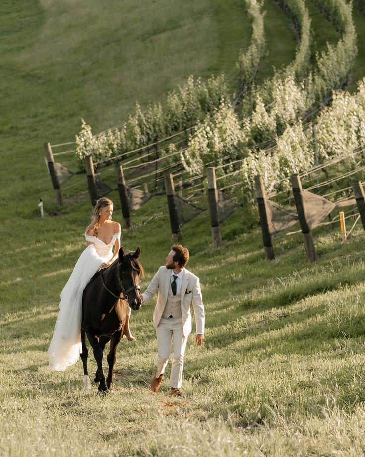 a bride and groom are walking with their horse in the field near some vines on a hill