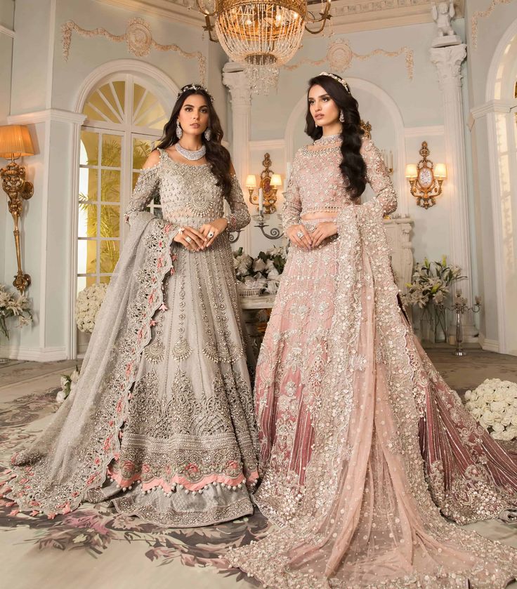 two women standing in front of a chandelier wearing long gowns and dresses