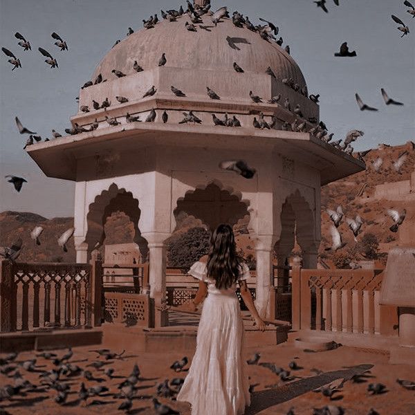 a woman standing in front of a white building surrounded by birds flying over her head