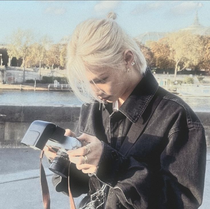 a woman is looking at her cellphone while standing on the sidewalk near water and trees