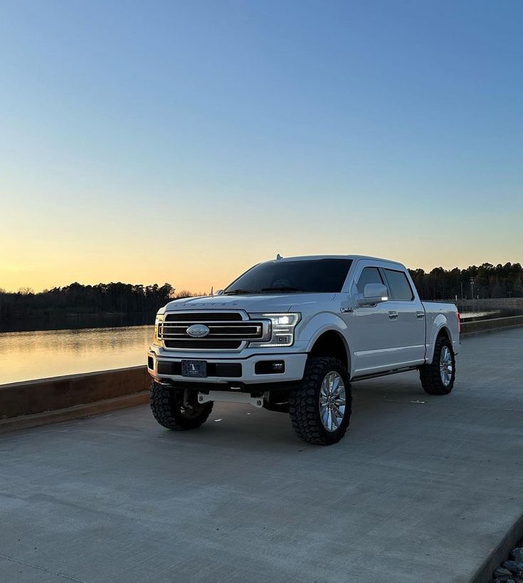 a white truck parked on the side of a road next to a body of water