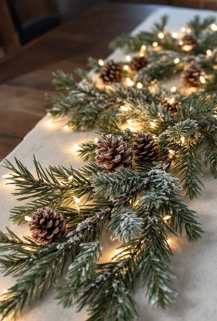 christmas garland with pine cones and lights on a white table cloth covered in snowflakes