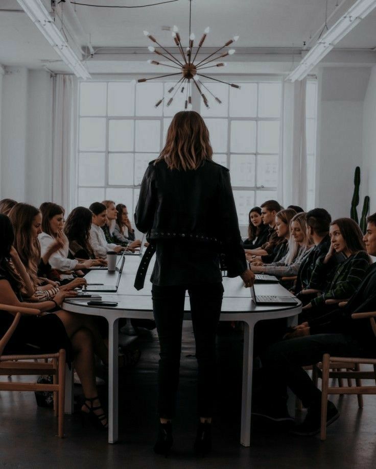 a woman standing at a table in front of a group of people sitting around it