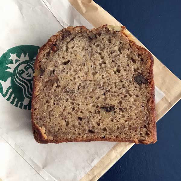 a loaf of banana bread sitting on top of a paper bag next to a starbucks cup