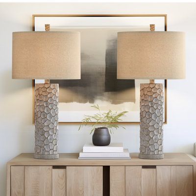 two lamps sitting on top of a wooden cabinet next to a painting and lamp shade