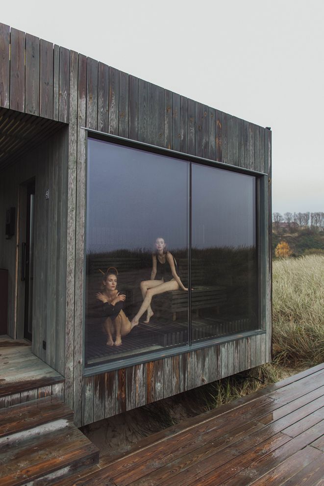 two people are reflected in the windows of a wooden building on a deck with wood planks