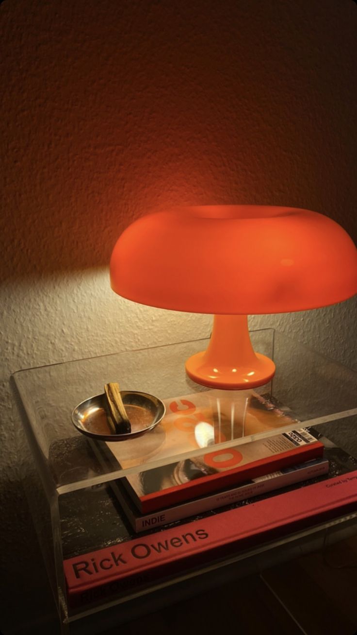 an orange lamp sitting on top of a table next to some books and a bowl