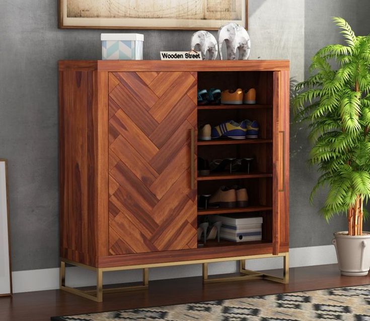 a wooden cabinet sitting next to a potted plant in front of a painting on the wall