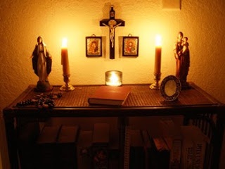 a shelf with candles and pictures on it in front of a wall mounted crucifix