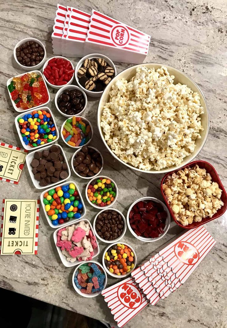 a table topped with bowls filled with different types of candy and popcorn next to boxes of snacks