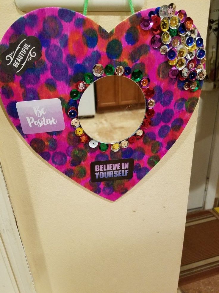 a heart shaped mirror hanging on the side of a wall with beads and jewels in it