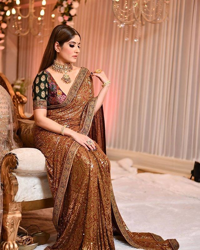 a woman in a brown sari sitting on a chair with chandelier behind her