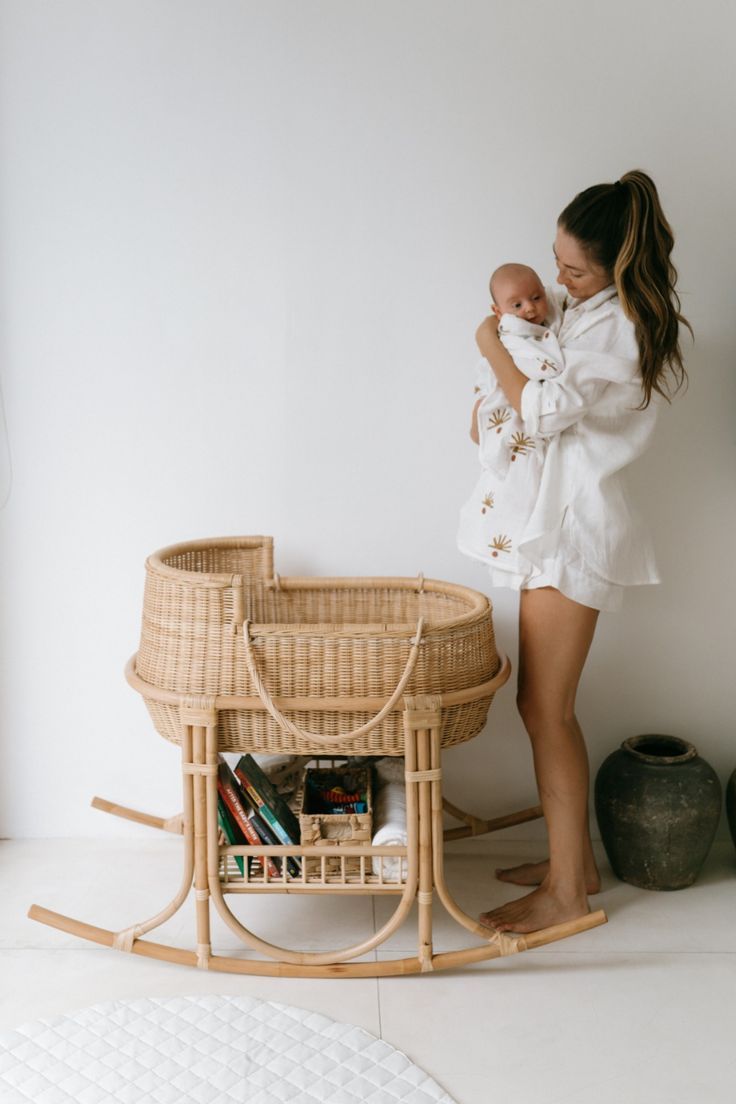 a woman standing next to a baby in a wicker bassinet and holding her infant