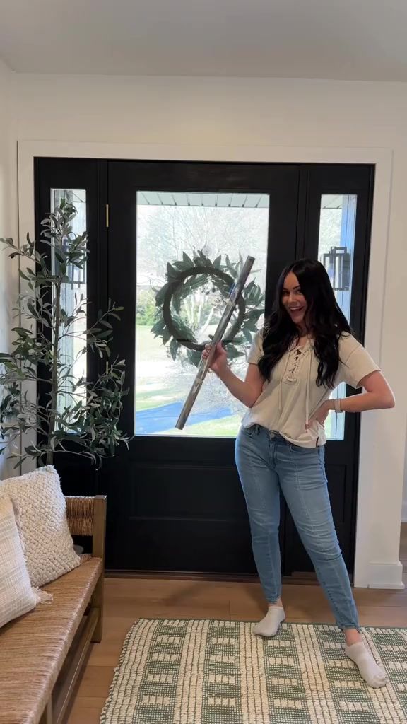 a woman standing in front of a black door holding a large metal object with one hand