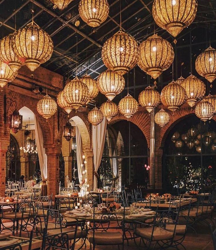 an indoor dining area with chandeliers hanging from the ceiling and tables set for dinner