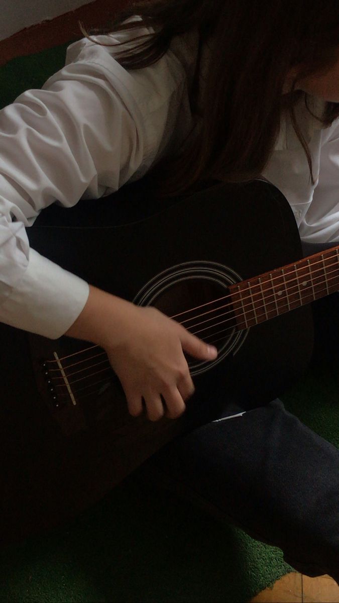 a woman sitting on the floor playing an acoustic guitar with her right hand and fingers