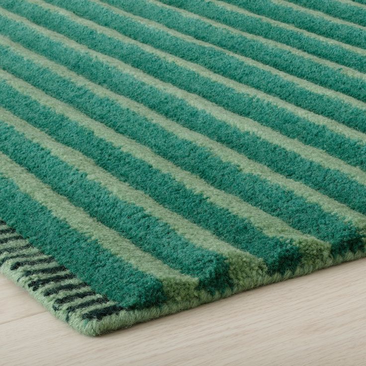 a green rug with black stripes on the top and bottom, sitting on a wooden floor