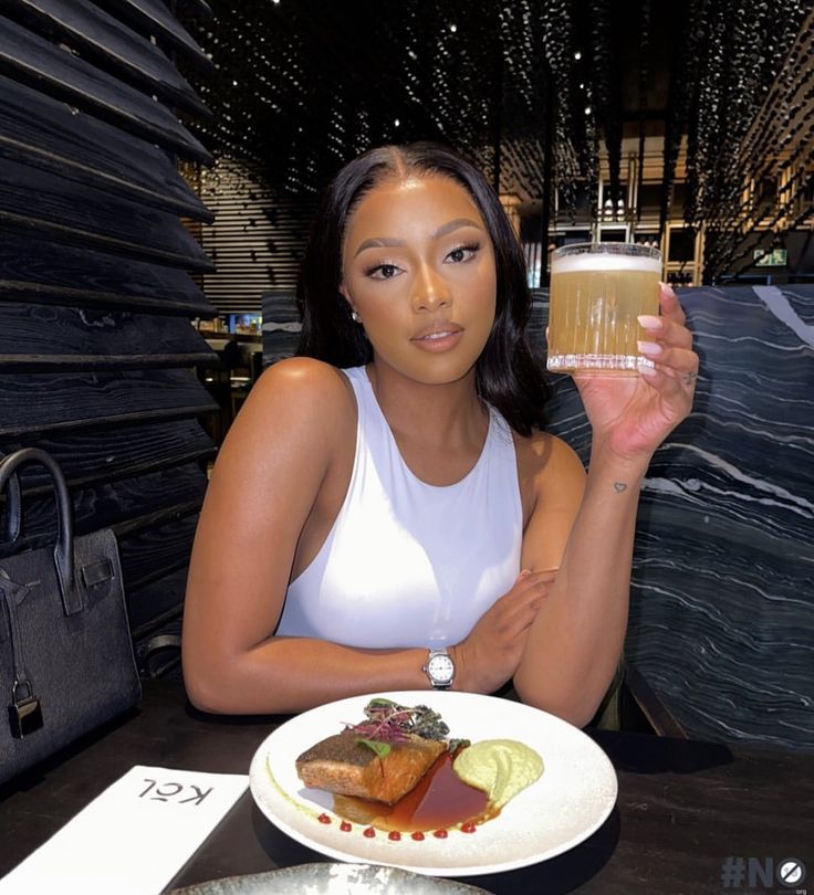 a woman sitting at a table with a plate of food and drink in her hand