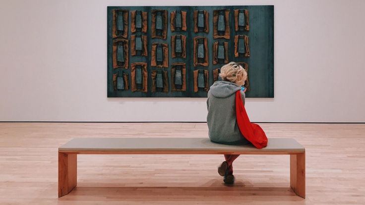 a woman sitting on top of a bench in front of a large piece of art