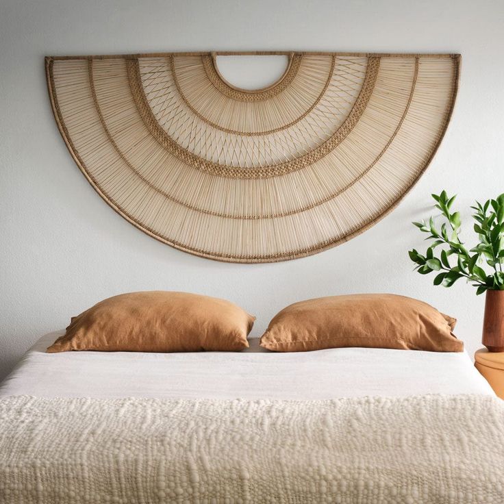 a bed with two pillows and a plant in front of the wall hanging above it