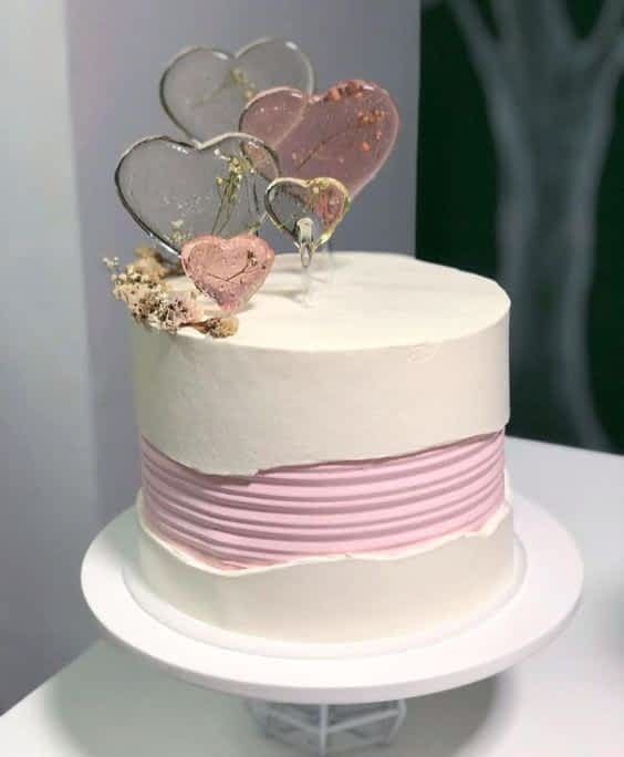 a white cake with pink icing and two hearts on top, sitting on a plate