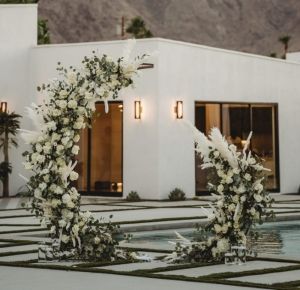 two white flowers and greenery are arranged in front of a house