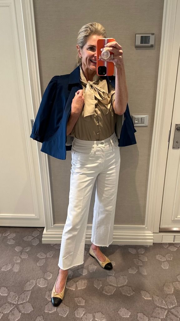 a woman taking a selfie in front of a door wearing white pants and a blue jacket