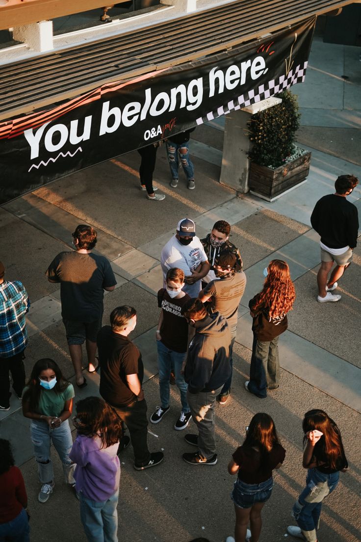 a group of people standing around each other in front of a sign that says you belong here