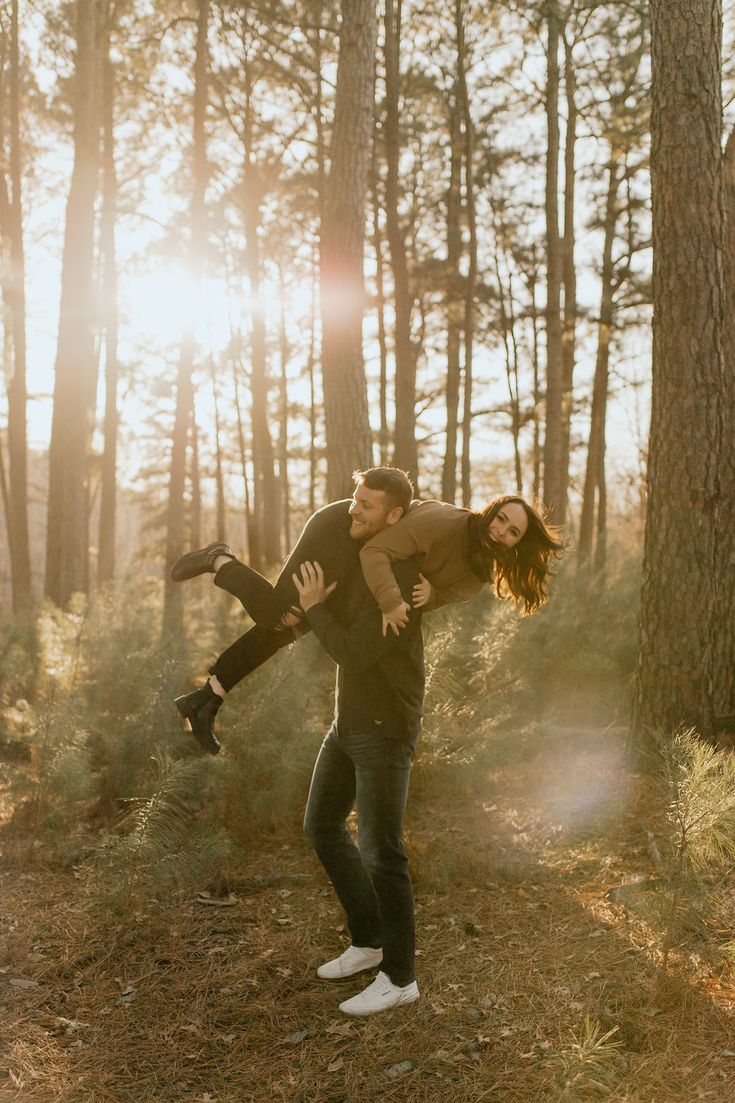 a man holding a woman in the air while standing next to some trees and grass