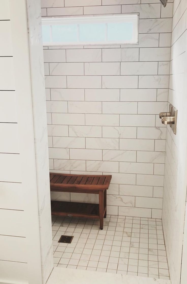 a white tiled bathroom with a bench in the shower