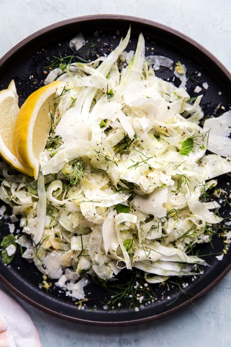 a black bowl filled with shaved cabbage and lemon wedges on top of a table