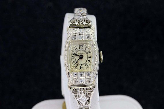 This wrist watch is a Robbins's that is 14K gold one piece case that has pave diamonds set around the watch.The diamonds are estimated to be a SI2 clarity and is a G/H color.The band is hinged and has filigree and pave set diamonds set on it. The face of the dial is engraved with daisies and leaves and has a domed crystal. The case of the watch is engraved with flowers and various other floral patterns.It has a clasp and safety latch to make it secure on the wrist. The case of the watch measures Anniversary Diamond Watch With Pave Setting, Timeless Diamond Watch For Wedding, Diamond Wedding Watch With Diamond Hour Markers, Wedding Diamond Watch With Diamond Hour Markers, Timeless Diamond Wedding Watches, Wedding Jewelry And Watches With Brilliant Cut Diamonds, Wedding Diamond Watch With Diamond Accents, Wedding Diamond Jewelry And Watches With Brilliant Cut, Wedding Diamond Jewelry With Brilliant Cut