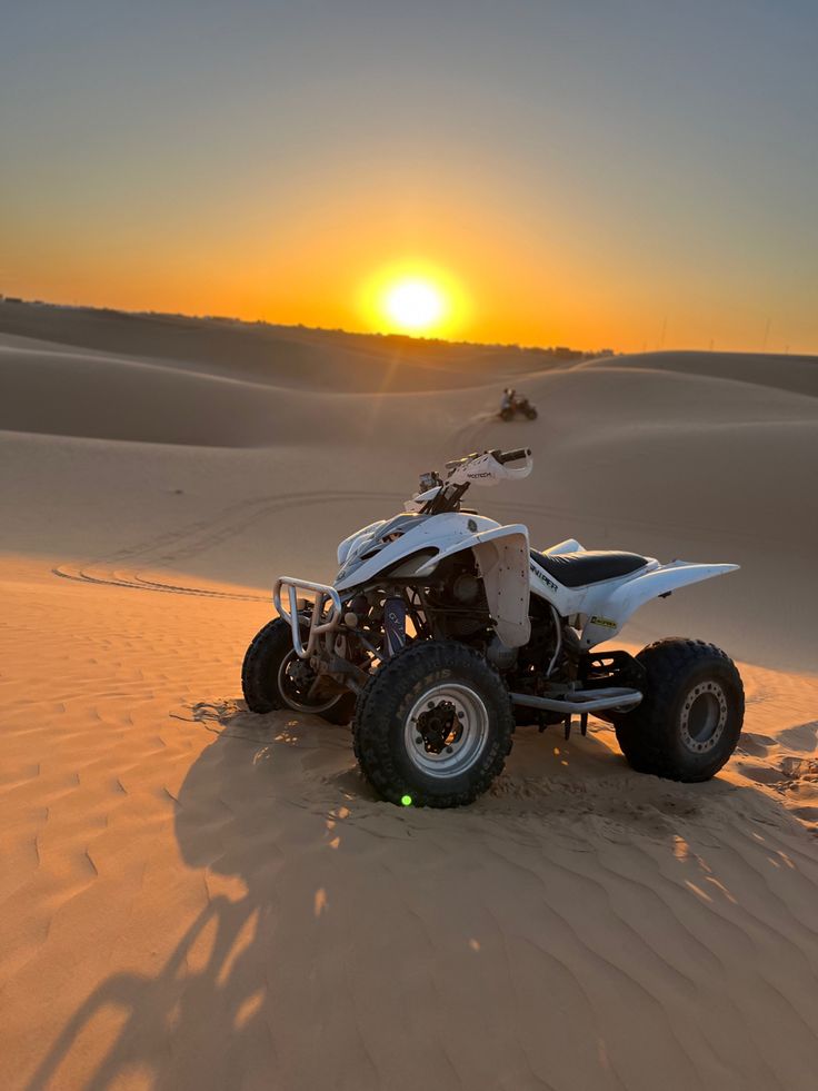 a white four - wheeler in the desert with the sun setting over the sand dunes