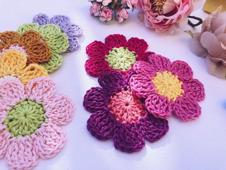 several crocheted flowers sitting on top of a table next to pink and yellow flowers