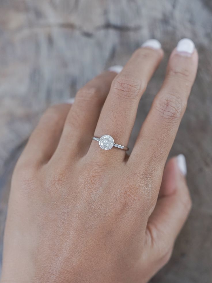 a woman's hand with a diamond ring on top of her left hand, against a rock surface