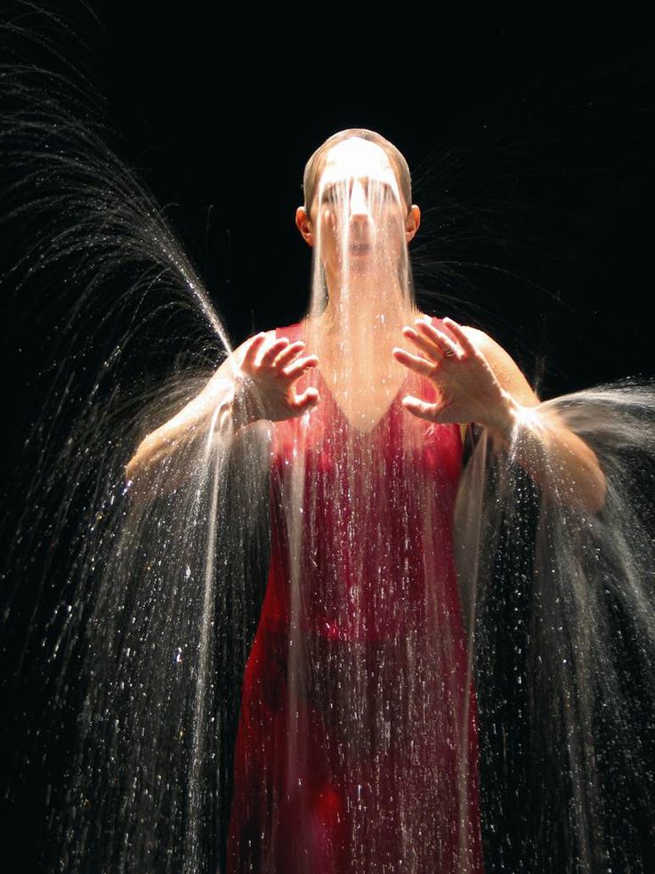 a woman standing in the rain with her hands on her head and hair flying out