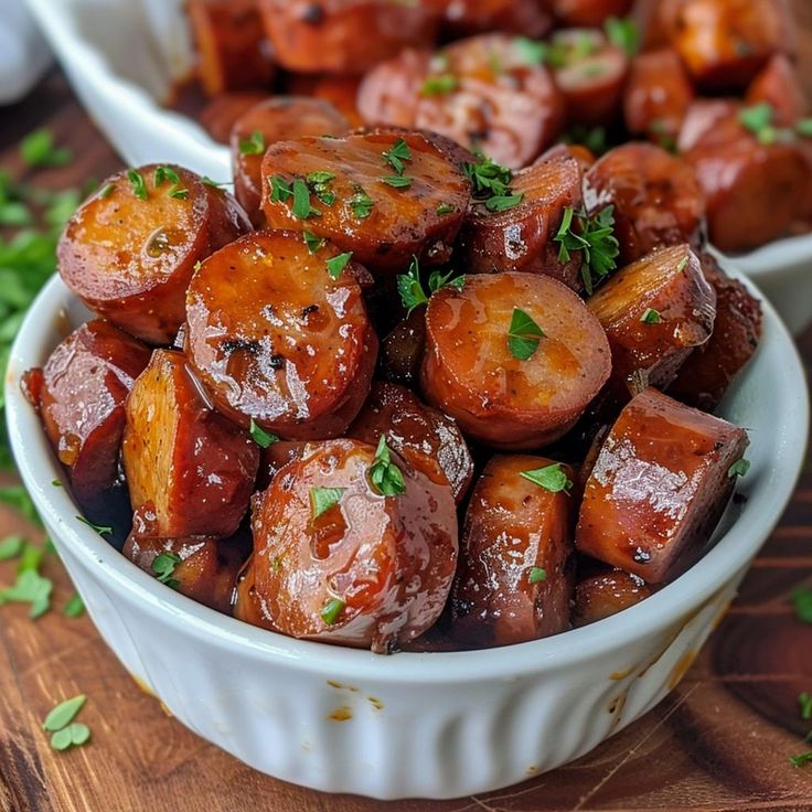 two white bowls filled with cooked carrots on top of a wooden table and garnished with parsley