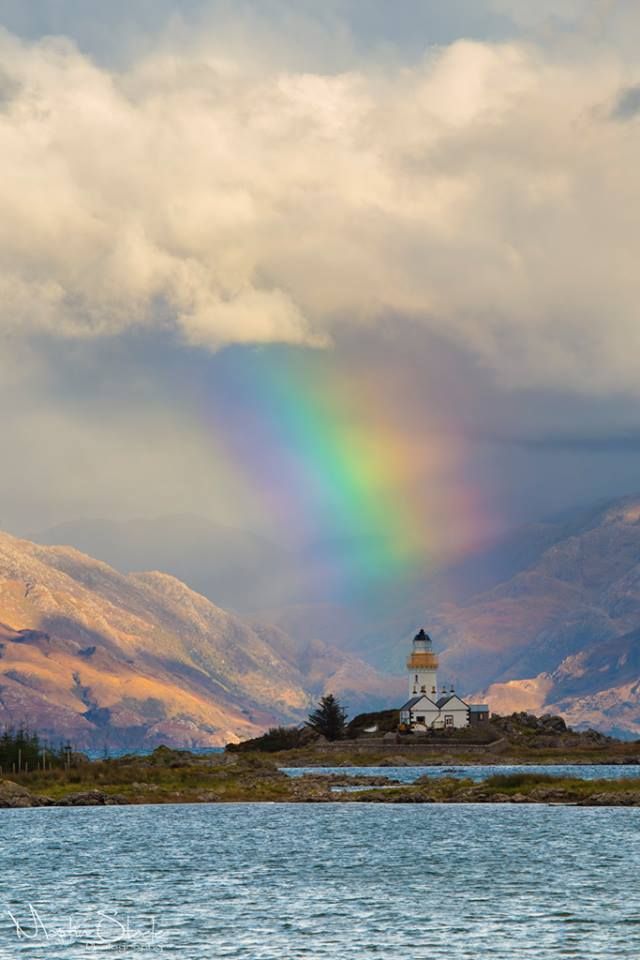 a rainbow shines in the sky over a small island with a lighthouse on it