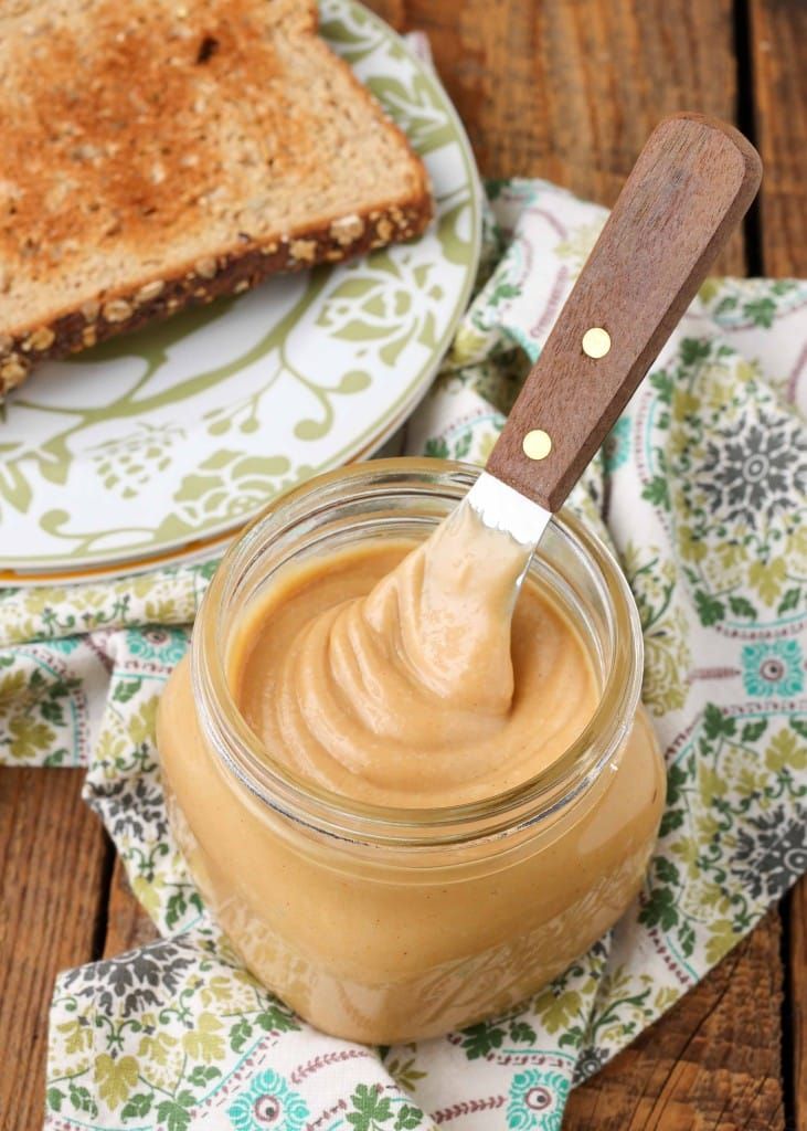 peanut butter in a glass jar with a wooden spoon on a plate next to it