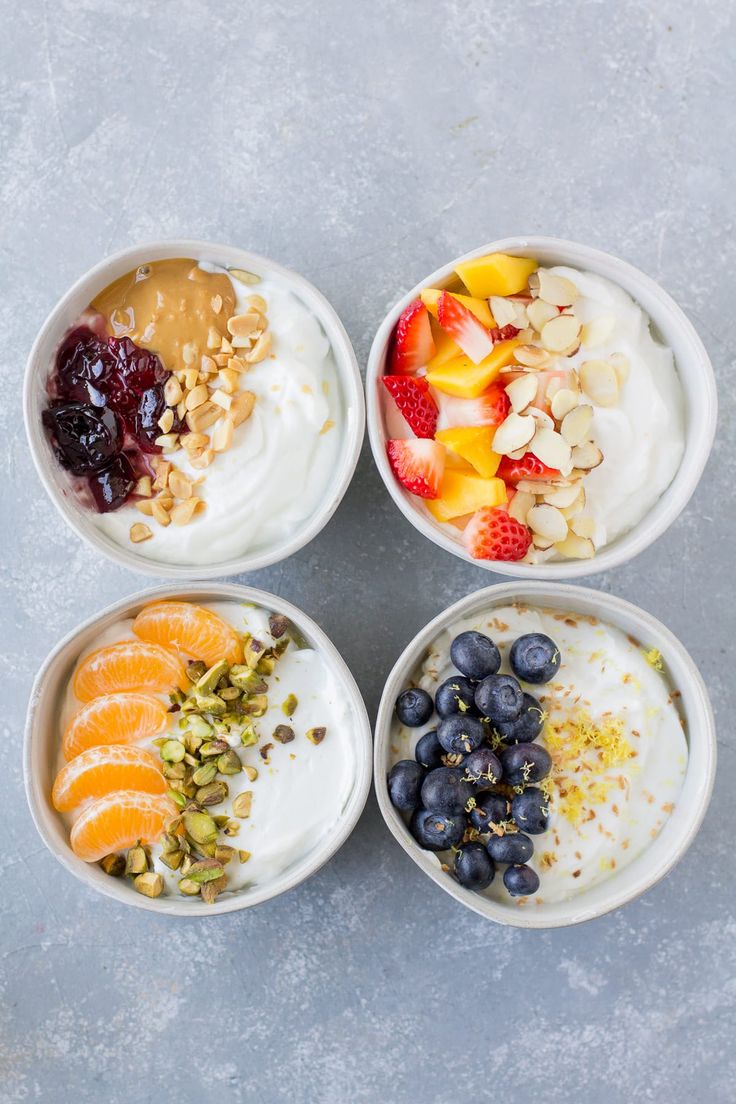 four bowls filled with fruit and yogurt on top of a gray countertop