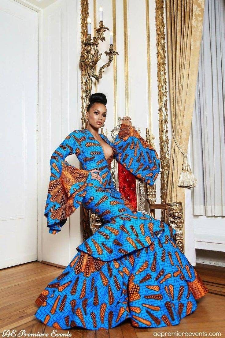 a woman in a blue and orange dress sitting on a chair with her arms outstretched