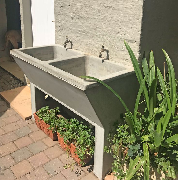 a concrete sink in front of a house with potted plants and brick walkway leading up to it