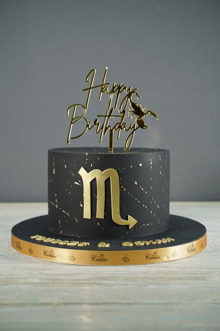 a black and gold happy birthday cake with the letter m on it's top