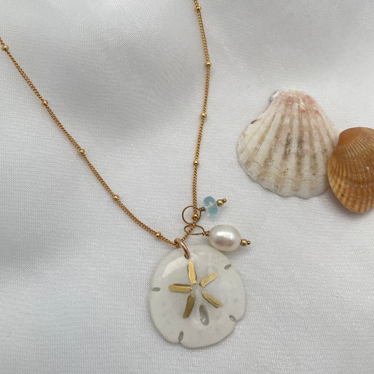 Legend has it that finding a sand dollar during a beach stroll is considered a lucky omen. So take a little bit of the beach and good luck with you wherever you go with our gorgeous Sand Dollar Charm Necklace. Features our most loved satellite chain, freshwater pearl, and blue zircon accents. Freshwater Baroque Pearl size: 6 to 8mm Blue Zircon roundel gemstone 4mm 14kt gold fill or sterling silver round beads 2mm 14kt gold fill or sterling silver satellite chain Real sand dollars are preserved a Beach Sand Necklace, Sand Dollar Jewelry, Gift Ocean-inspired Shell Necklace With Starfish Charm, Ocean-inspired Pearl Charm Jewelry For Beach, Dainty Starfish Necklace For Beach, Ocean-inspired Starfish Shell Necklace As Gift, Ocean-inspired Starfish Shell Necklace, Dainty Pearl Charm Necklace For The Beach, White Ocean-inspired Charm Necklace For Gift