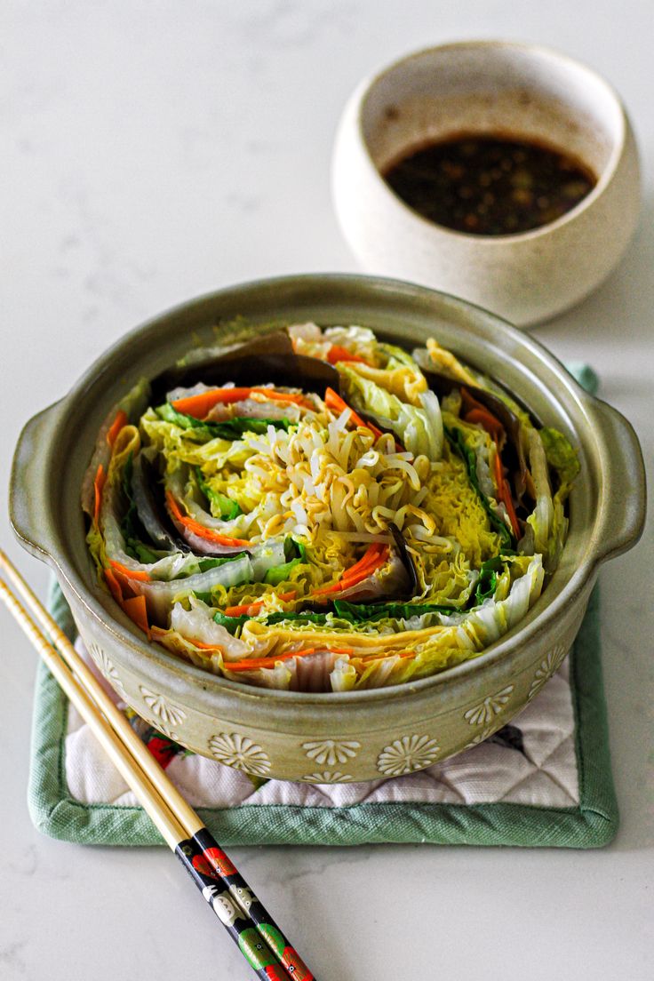 a bowl filled with vegetables next to chopsticks on a napkin and saucer