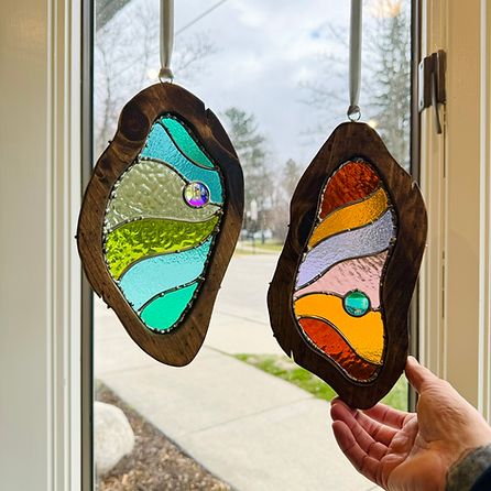 two stained glass hangings in front of a window with a hand holding it up